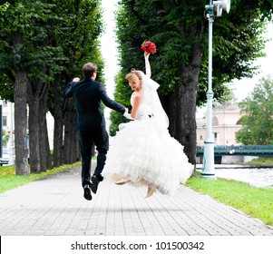 bride and groom is running with joined hands on city park road