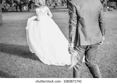 Bride And Groom Running On Green Grass Of Golf Course, Back View. Happy Wedding Couple Walking In The Forest. Black And White Photo