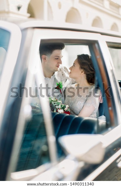 Bride with groom sitting in old\
black retro car. Newlyweds kissing and embracing while sitting\
inside old black retro car in old city center. Lviv,\
Ukraine.