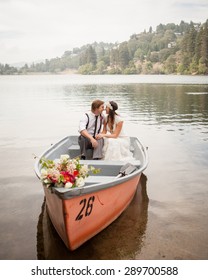 Bride and groom sitting in an orange row boat on the lake kissing