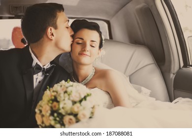 Bride and groom sitting in the vintage car and going for a kiss. Romantic moment.