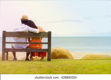 A bride and groom sitting wooden bench on the beach - Powered by Shutterstock