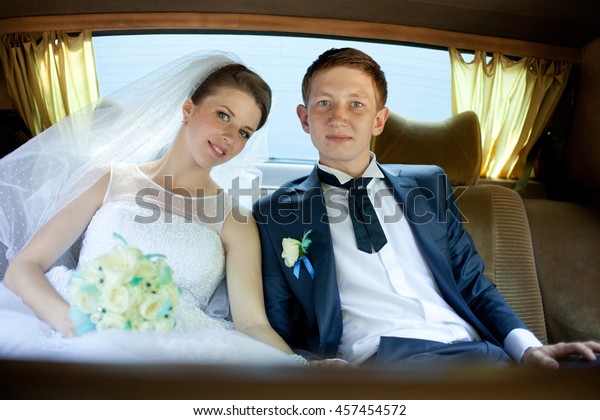 Bride and\
groom smile while sitting on the back\
seat