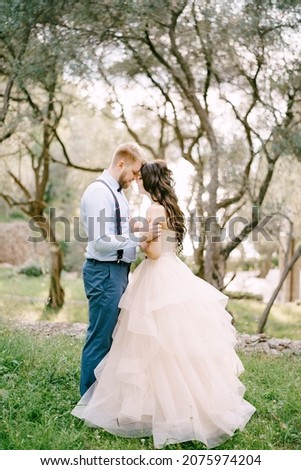 The bride and groom stand hugging among the trees in the olive grove 