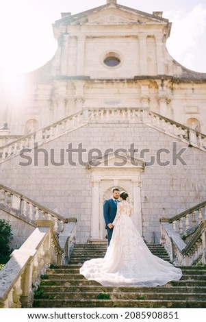 Bride and groom stand on the stone steps near the ancient church