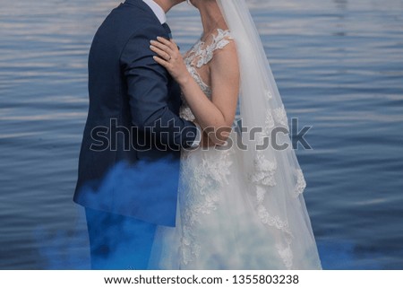 bride and groom stand together against the water