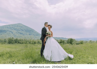 A bride and groom are standing in a field with a beautiful view of the mountains in the background - Powered by Shutterstock