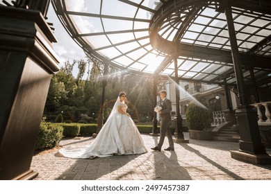 A bride and groom are standing in front of a building with a large archway. The bride is wearing a white dress and the groom is wearing a suit. Scene is romantic and happy - Powered by Shutterstock