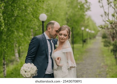 A bride and groom are standing in a garden, with the bride wearing a white dress and the groom wearing a blue suit - Powered by Shutterstock