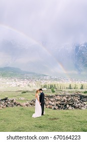 Bride and groom standing in the mountains with rainbow background