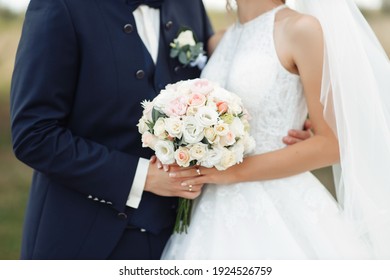 The bride and groom are standing next to each other and a man in a blue stylish suit with a bow-tie gently holds her by the shoulders. Girl in a white dress with a bouquet of roses flowers in her hand - Powered by Shutterstock