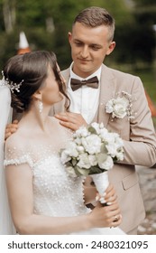 A bride and groom are standing together, the bride holding a bouquet and the groom wearing a suit