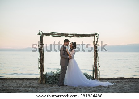 The bride and groom under archway on beach. Sunset, twilight.