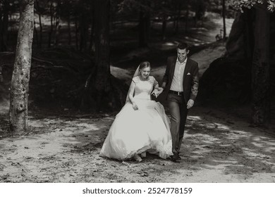 A bride and groom are walking down a path in the woods. The bride is wearing a white dress and the groom is wearing a suit. Scene is romantic and happy