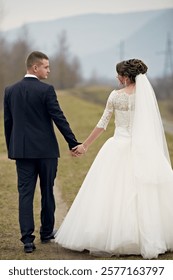 A bride and groom are walking down a path in the woods. The bride is wearing a white dress and the groom is wearing a suit. They are holding hands and seem to be enjoying their time together