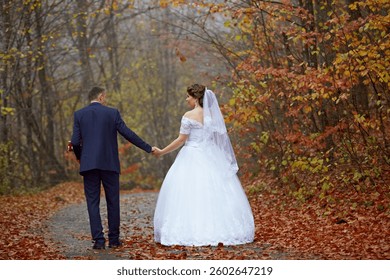 A bride and groom are walking down a path in the woods. The bride is wearing a white dress and the groom is wearing a suit. Scene is romantic and peaceful