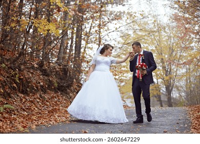 A bride and groom are walking down a path in the woods. The bride is wearing a white dress and the groom is wearing a suit. They are holding hands and the bride is touching the groom's face