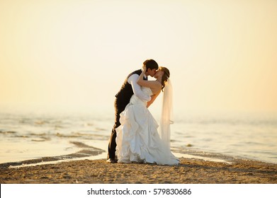 bride and groom walking on the sand at sunset