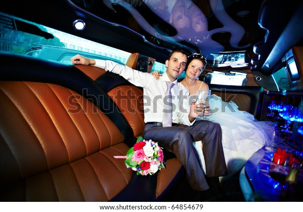 Bride and groom in wedding limousine with\
glasses of champagne