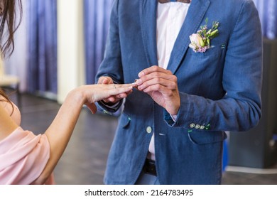 Bride And Groom. Wedding Ring And Wedding Bouquet. Spring Summer Celebration. He Puts A Ring On Her Hand. Blue Wedding Suit. Purple Bouquet And Gold Rings.