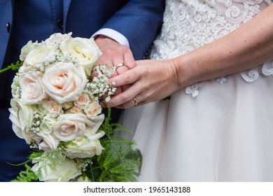 Bride And Groom's Hands Golden Rings On Fingers, Holding Blush Pink  Roses  Wedding Bouquet, Cream Vintage Lace Wedding Dress, Dark Blue Suit