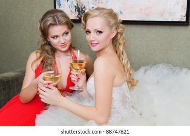 The bride and her bridesmaid with a glass of wine on the sofa