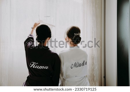 A bride with her maid of honor, wearing wedding robe with names on it, get ready for the wedding day