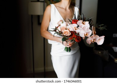 Bride hold the bouquet in her hands. Standing by the window.