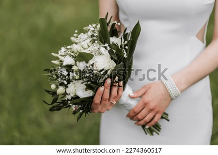 The bride is holding a beautiful wedding bouquet of white flowers. White evening dress, beautiful jewelry on the hand