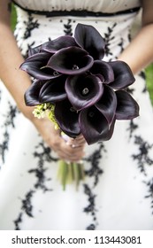 bride holding a bouquet of purple callas, wearing a weddingdress with dark lace