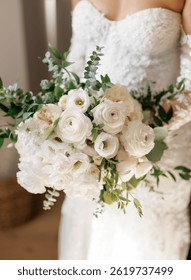 Bride holding a bouquet of white flowers in the room close-up. Beautiful wedding bouquet of white flowers, roses and eucalyptus leaves in the hands of the bride. Details of the wedding morning