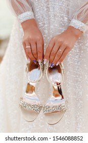 A bride holding gorgeous wedding shoes.Morning bride. Bride in wedding dress holding a shoes looking out the window morning preparation for wedding ceremony.