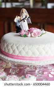 Bride Holding Gun To Groom With Hands Behind Head Funny Wedding Cake Topper With Pink Roses Closeup And Cupcakes On Table