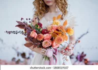 Bride holds beautiful autumn bouquet with orange and red flowers and berries. Autumn bouquet with ribbons in bride's hands