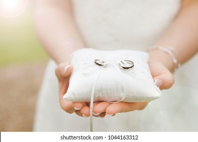 A bride holds a ring pillow with the new wedding rings in her hands - Powered by Shutterstock