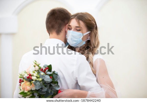 The\
bride in a medical mask with a bouquet of flowers is dancing with\
the groom. Wedding during the coronavirus\
panademia.
