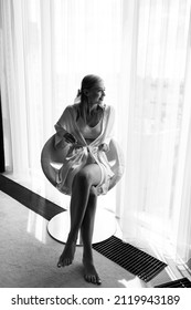 Bride morning. A girl in a white peignoir sits on a chair. Glamorous photo shoot by the window. Black and white photo.