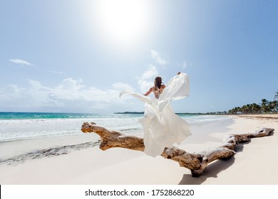 Bride on the beach back view in a white wedding dress walking on the white sandy caribbean beach landscape on  sunny day in Dominican republic 