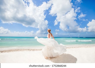 Bride on the beach back view in a white wedding dress walking on the white sandy caribbean beach landscape on  sunny day in Dominican republic 