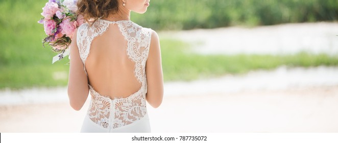 Bride On The Beach. Woman Holding  Bouquet Of Pink Flowers. Open Back Wedding Dress.  Coast Of The Sea. Copy Space.