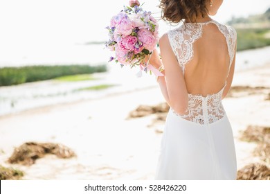 Bride on the coast of the sea. On the bride is a long wedding dress with lace and an open back. - Shutterstock ID 528426220