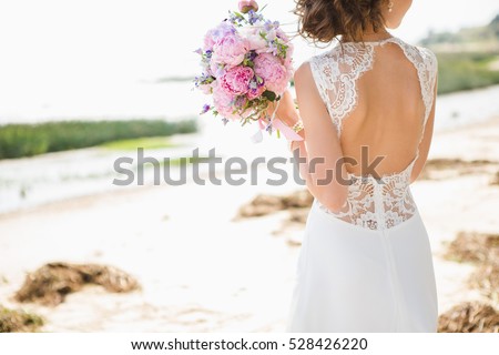 Bride on the coast of the sea. On the bride is a long wedding dress with lace and an open back.