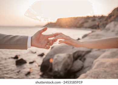 a bride placing her hand on the groom's hand and wedding rings visible on both hands. Fingertips touching. sunset and sea in the background - Powered by Shutterstock