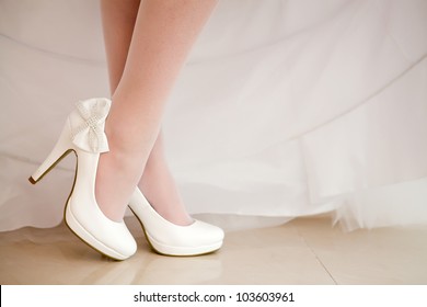 The bride shows white wedding shoes