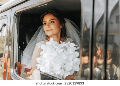 the bride sits in a black car on the wedding day with a bouquet. Portrait of the bride. lush white lace dress