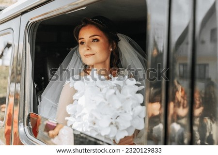 the bride sits in a black car on the wedding day with a bouquet. Portrait of the bride. lush white lace dress