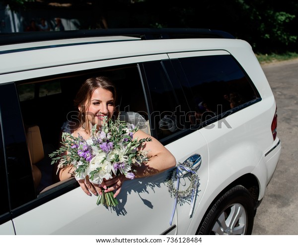 Bride\
sits with white and violet bouquet in the\
limousine