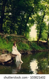 A bride sitting on a rock on a riverbank