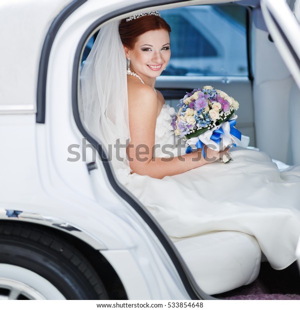 bride sitting in wedding car, holding bouquet of\
various flowers