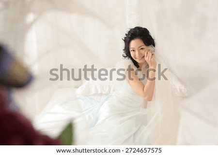 Bride smiling in light room while preparing for wedding ceremony with veil and soft fabrics surrounding her
